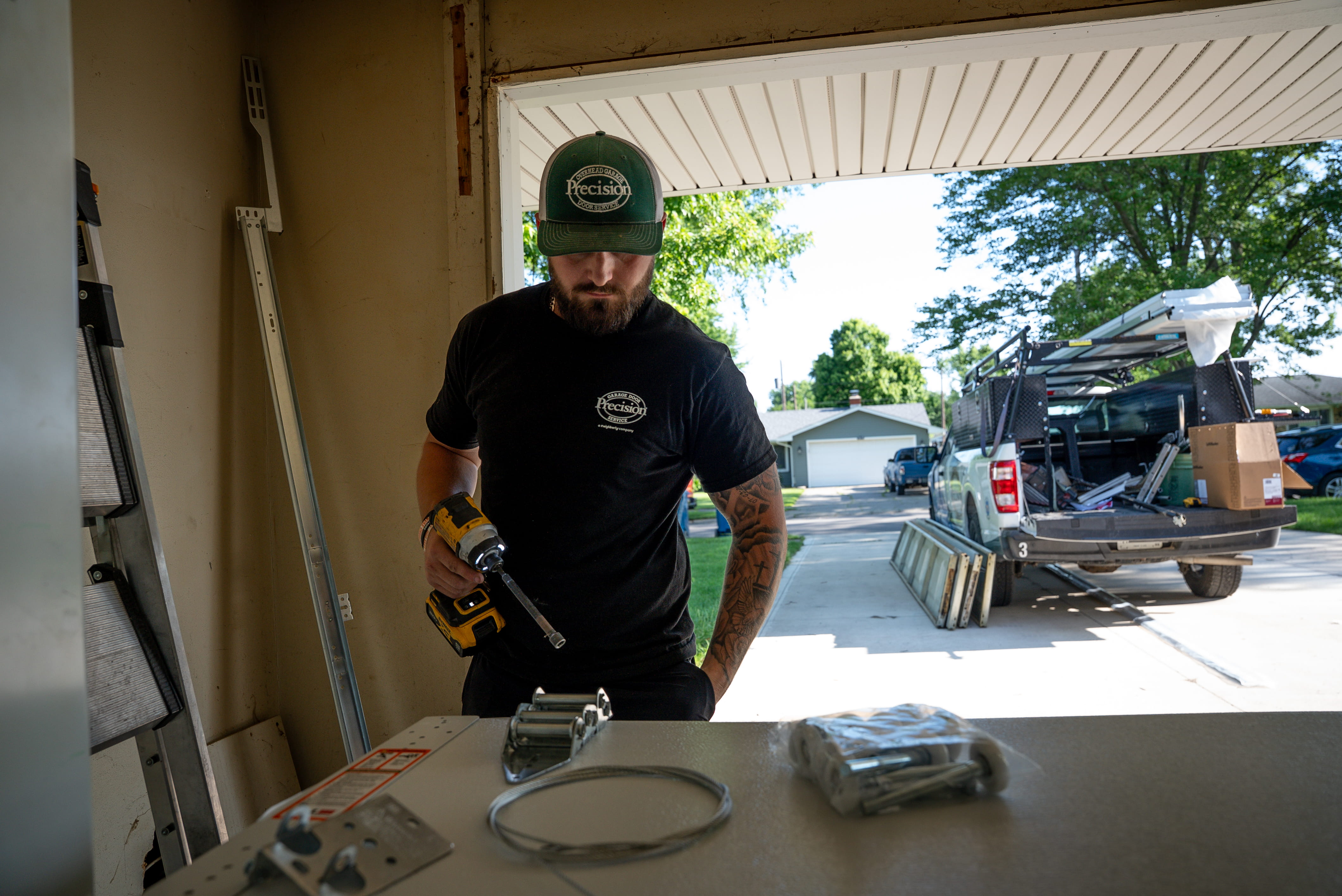 Technician Working on Garage Door Parts with Vehicle Behind Him Technician Working on Garage Door Parts with Vehicle Behind Him